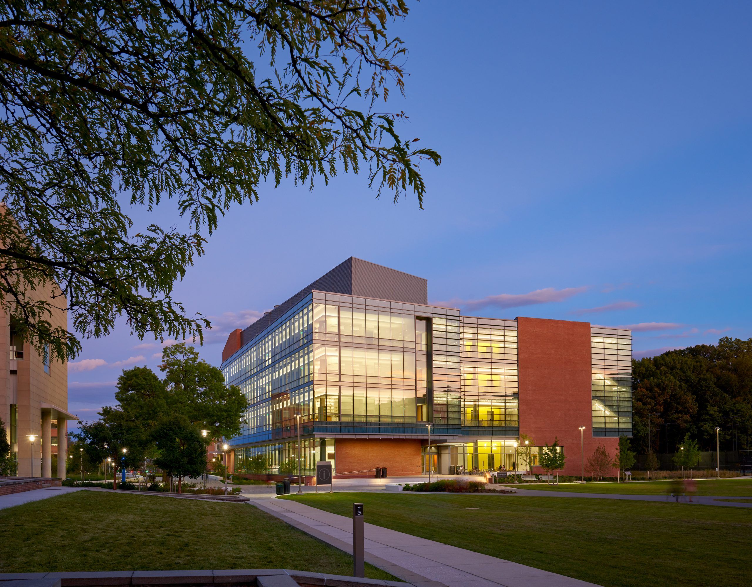 Exterior shot of the ISLB at dusk, with windows lit and a pathway leading calmly up to its main campus entrance across the student green